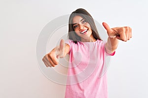 Young beautiful woman wearing pink casual t-shirt standing over isolated white background approving doing positive gesture with