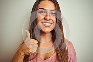 Young beautiful woman wearing pink t-shirt standing over isolated white background happy with big smile doing ok sign, thumb up