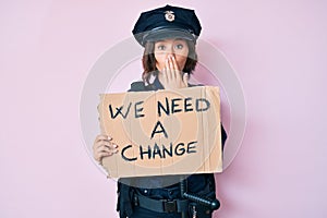 Young beautiful woman wearing police uniform holding we need a change banner covering mouth with hand, shocked and afraid for