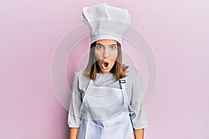 Young beautiful woman wearing professional cook uniform and hat afraid and shocked with surprise expression, fear and excited face