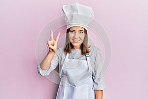 Young beautiful woman wearing professional cook uniform and hat showing and pointing up with fingers number two while smiling