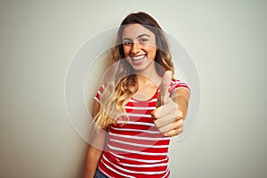 Young beautiful woman wearing red stripes t-shirt over white isolated background doing happy thumbs up gesture with hand