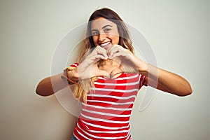 Young beautiful woman wearing red stripes t-shirt over white isolated background smiling in love showing heart symbol and shape