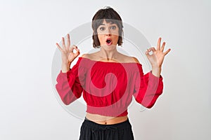 Young beautiful woman wearing red summer t-shirt standing over isolated white background looking surprised and shocked doing ok