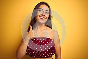 Young beautiful woman wearing red t-shirt standing over isolated yellow background doing happy thumbs up gesture with hand
