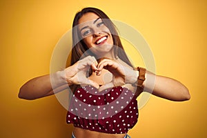 Young beautiful woman wearing red t-shirt standing over isolated yellow background smiling in love showing heart symbol and shape