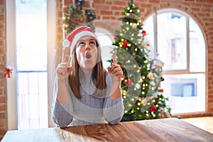 Young beautiful woman wearing santa claus hat at the table at home around christmas decoration amazed and surprised looking up and