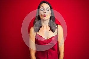 Young beautiful woman wearing sexy lingerie over red isolated background making fish face with lips, crazy and comical gesture