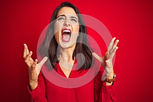 Young beautiful woman wearing shirt standing over red isolated background crazy and mad shouting and yelling with aggressive