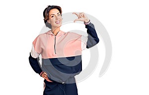 Young beautiful woman wearing sportswear smiling and confident gesturing with hand doing small size sign with fingers looking and