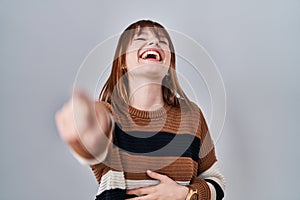 Young beautiful woman wearing striped sweater over isolated background laughing at you, pointing finger to the camera with hand