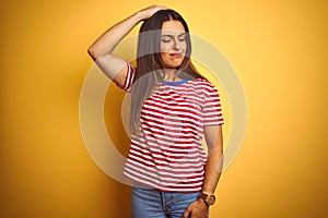 Young beautiful woman wearing striped t-shirt standing over isolated yellow background confuse and wonder about question