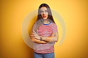 Young beautiful woman wearing striped t-shirt standing over isolated yellow background skeptic and nervous, disapproving