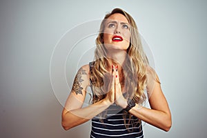 Young beautiful woman wearing stripes t-shirt standing over white isolated background begging and praying with hands together with