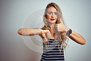 Young beautiful woman wearing stripes t-shirt standing over white isolated background Doing thumbs up and down, disagreement and