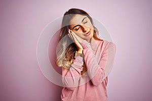 Young beautiful woman wearing a sweater over pink  background sleeping tired dreaming and posing with hands together while