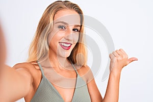 Young beautiful woman wearing t-shirt make selfie by camera over isolated white background pointing and showing with thumb up to