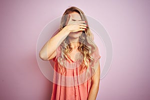 Young beautiful woman wearing t-shirt standing over pink isolated background covering eyes with hand, looking serious and sad