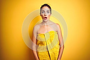 Young beautiful woman wearing towel after shower over yellow isolated background afraid and shocked with surprise expression, fear