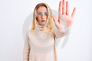 Young beautiful woman wearing turtleneck sweater standing over isolated white background doing stop sing with palm of the hand