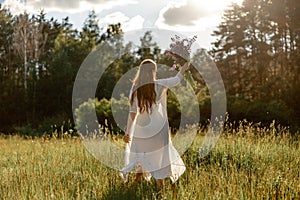 Young beautiful woman, wearing white dress, holding flowers and dancing on the meadow. Girl joying nature and freedom