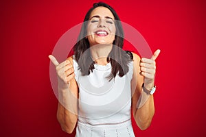 Young beautiful woman wearing white dress standing over red isolated background success sign doing positive gesture with hand,