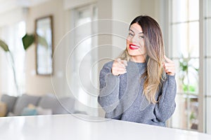 Young beautiful woman wearing winter sweater at home pointing fingers to camera with happy and funny face