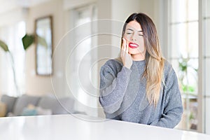 Young beautiful woman wearing winter sweater at home touching mouth with hand with painful expression because of toothache or