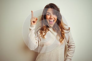 Young beautiful woman wearing winter sweater standing over white isolated background pointing finger up with successful idea