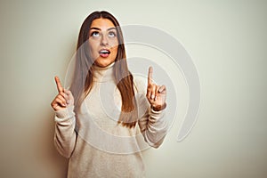 Young beautiful woman wearing winter turtleneck sweater over isolated white background amazed and surprised looking up and