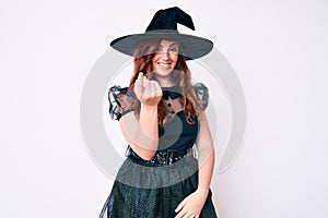 Young beautiful woman wearing witch halloween costume beckoning come here gesture with hand inviting welcoming happy and smiling