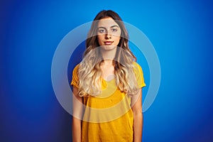 Young beautiful woman wearing yellow t-shirt over blue isolated background with serious expression on face