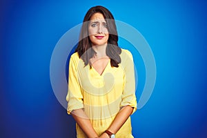 Young beautiful woman wearing yellow t-shirt standing over blue isolated background depressed and worry for distress, crying angry