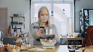 Young beautiful woman weighs the cocoa, adds to flour. Girl using kitchen scales, bowl and sieve for this.