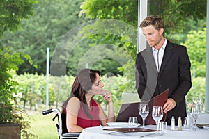 Young beautiful woman in wheelchair ordering at resturant