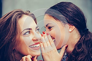 Young beautiful woman whispering something to her friends ear in a cafe