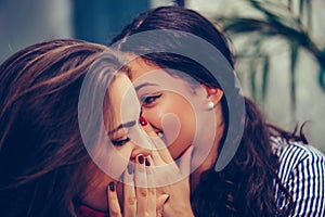 Young beautiful woman whispering something to her friends ear in a cafe