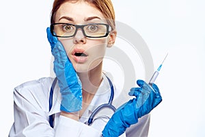 Young beautiful woman on white background in medical dressing gown and wearing glasses holds syringe, medicine, doctor