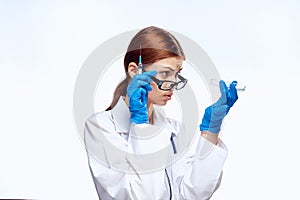 Young beautiful woman on white background in medical gown and glasses holds syringe and tests, medicine, doctor