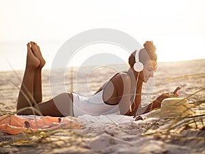 Woman in Bikini with a Smartphone and Headphones on the Beach