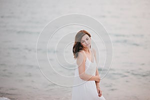 Young beautiful woman in a white dress walking on an empty beach near ocean