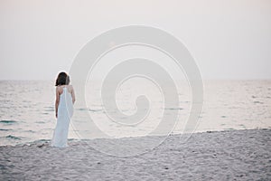 Young beautiful woman in a white dress walking on an empty beach near ocean