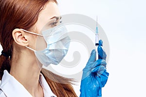 Young beautiful woman on white isolated background holds a syringe in a medical mask