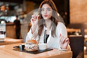 Young beautiful woman in white stylish blouse eating meat burger and fries for lunch in trendy cafe modern businesswoman