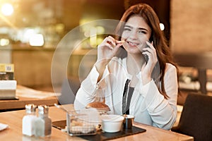 Young beautiful woman in white stylish blouse looks hungry eating meat burger with fries for lunch in trendy cafe while having