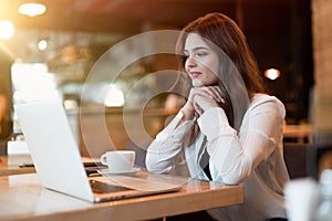 Young beautiful woman in white stylish jacket working in her laptop outside office during coffee break in cafe modern