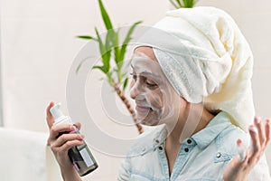A young beautiful woman with a white towel on her head in the bathroom applied makeup remover to her face against the background o
