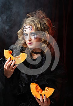 Young beautiful woman in a witch costume with bright makeup and hairstyle holding a pumpkin, a symbol of halloween.