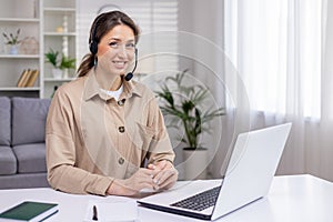 Young beautiful woman working from home remotely, businesswoman smiling and looking at camera, using headset phone and