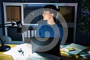 Young beautiful woman working at the office at night looking to side, relax profile pose with natural face with confident smile